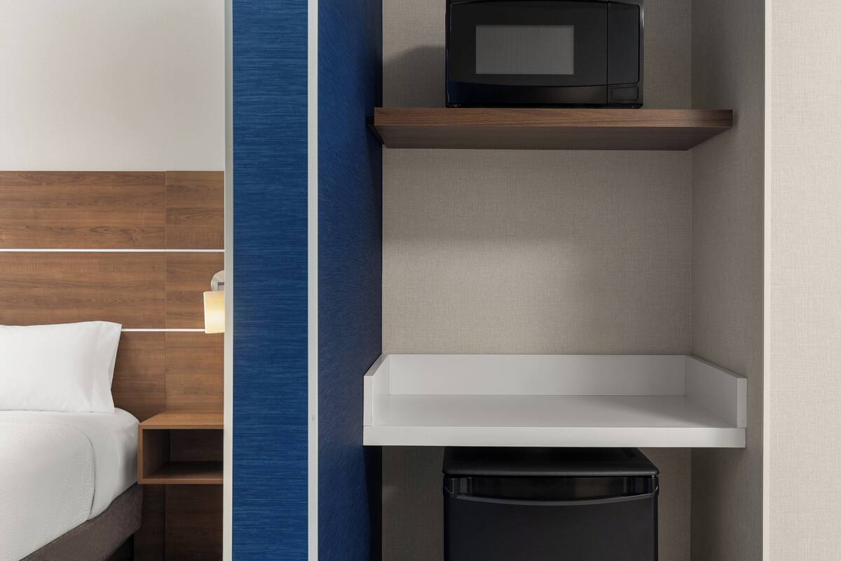 Une chambre d’hôtel avec un lit, une table de chevet, un four à micro-ondes posé sur une étagère et une poubelle.