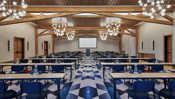 A conference room with tables, chairs, a projector screen, and chandeliers.