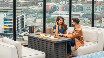 A modern indoor seating area with a fireplace, a city view, and a glass table with drinks.