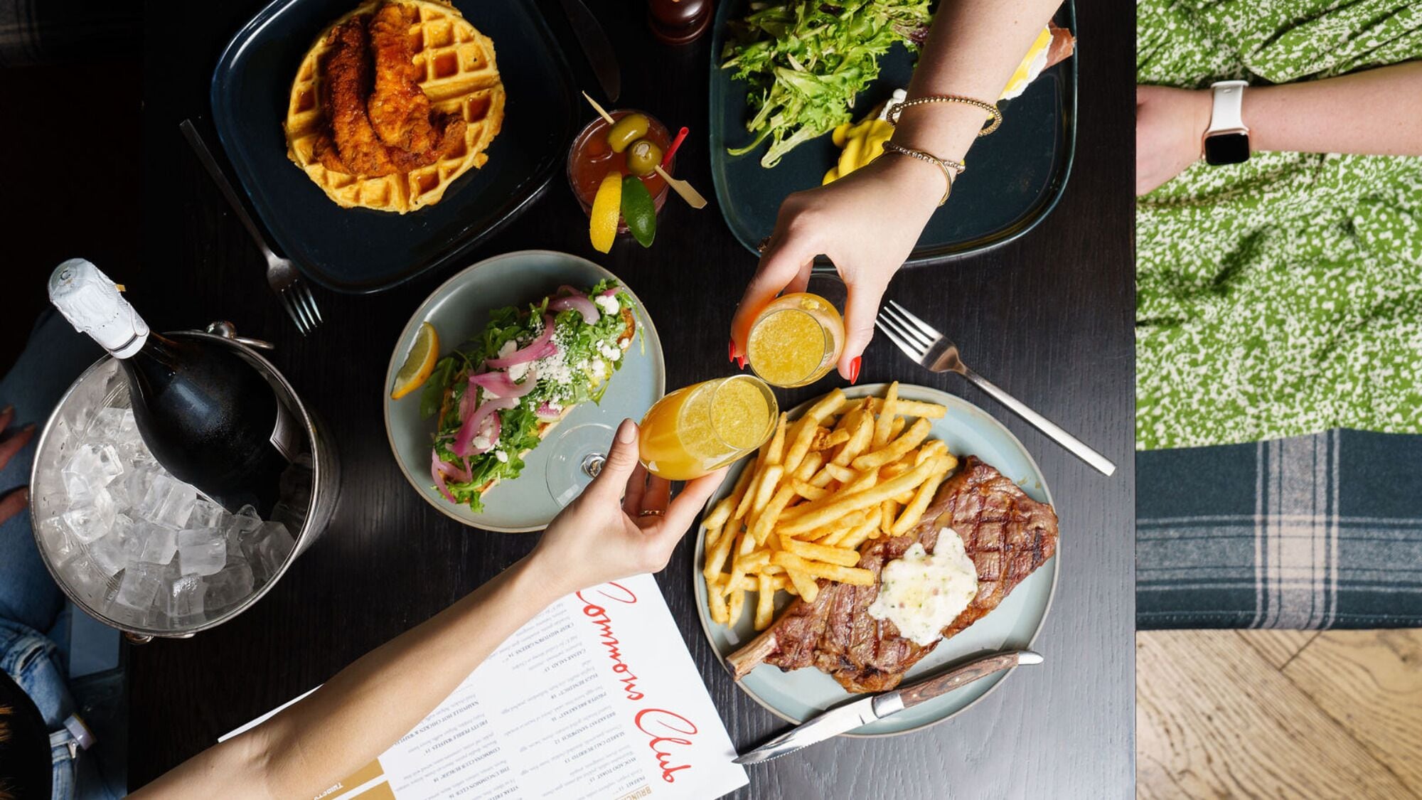 Una mesa de comedor con varios platos, incluyendo un gofre, ensalada, bistec y papas fritas.