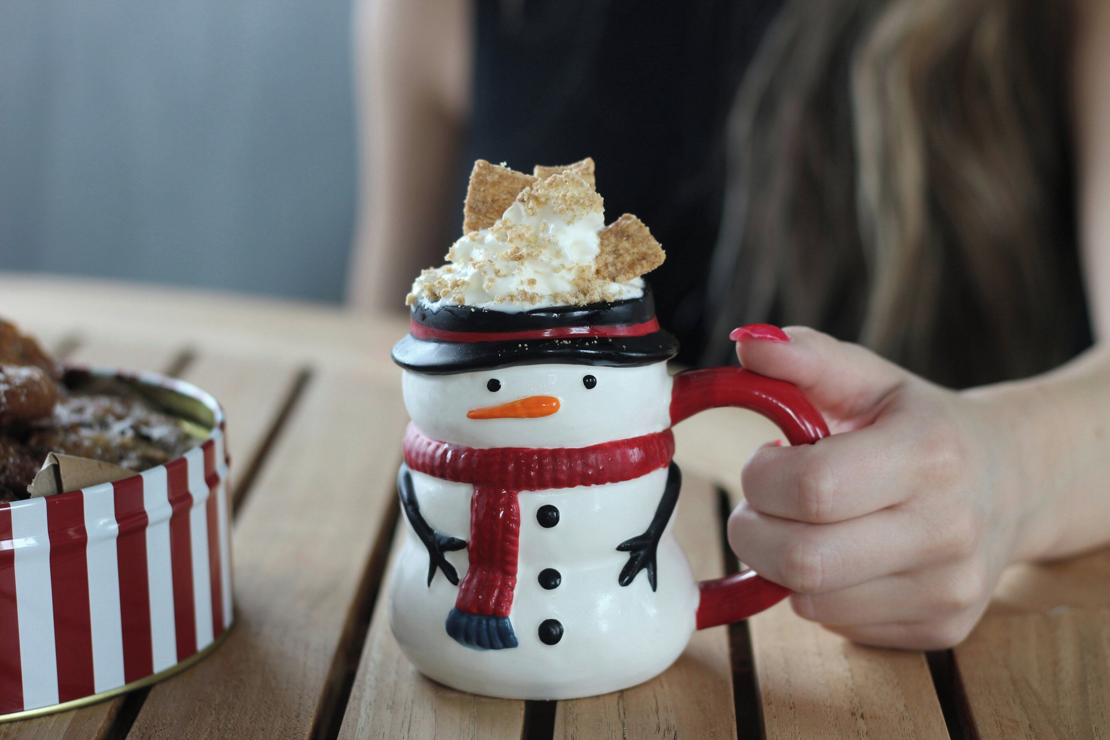 Eine Schneemann-Tasse mit rotem Schal und einem Stück Kuchen darauf.
