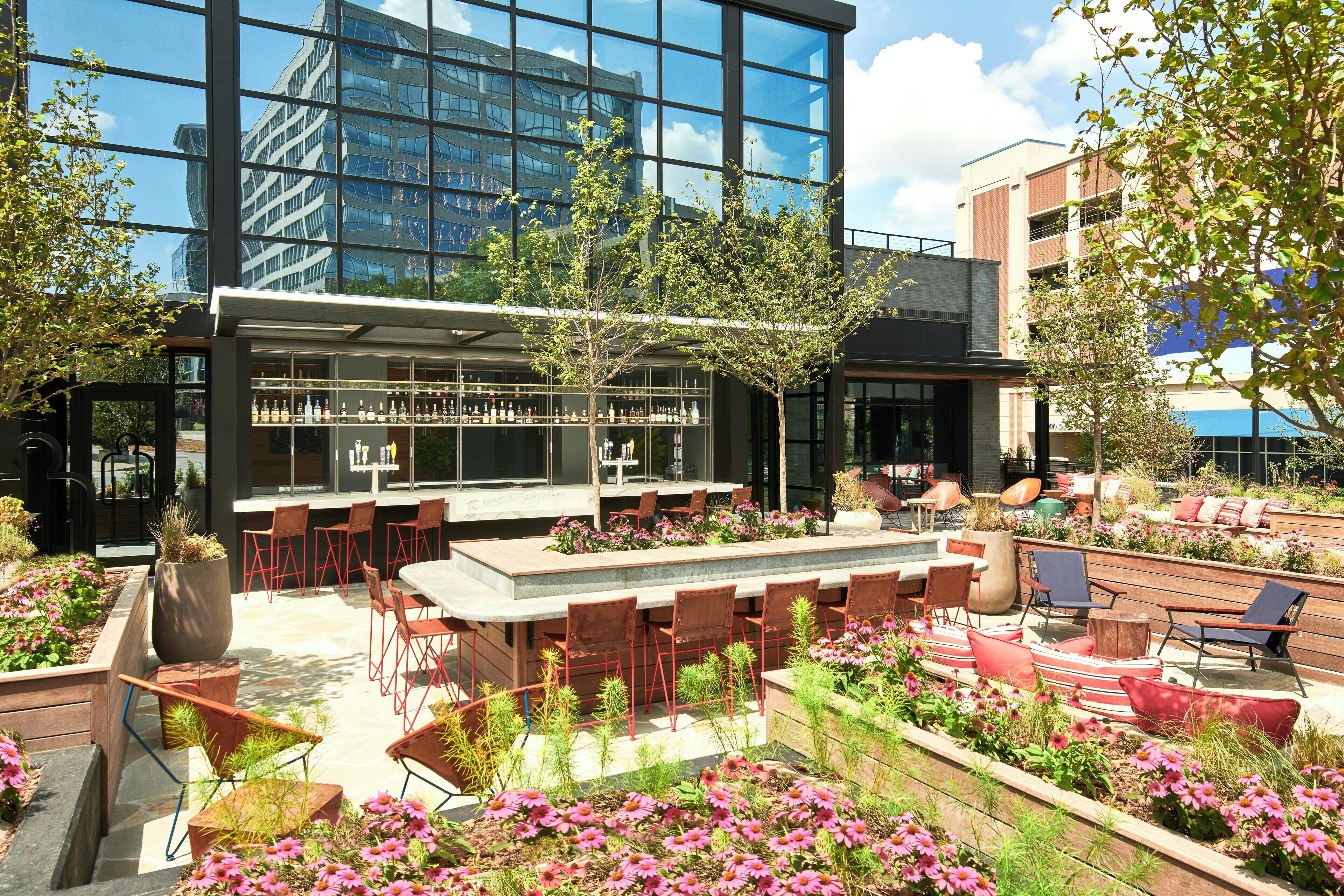 An outdoor seating area with a bar, red chairs, and a variety of plants and flowers.