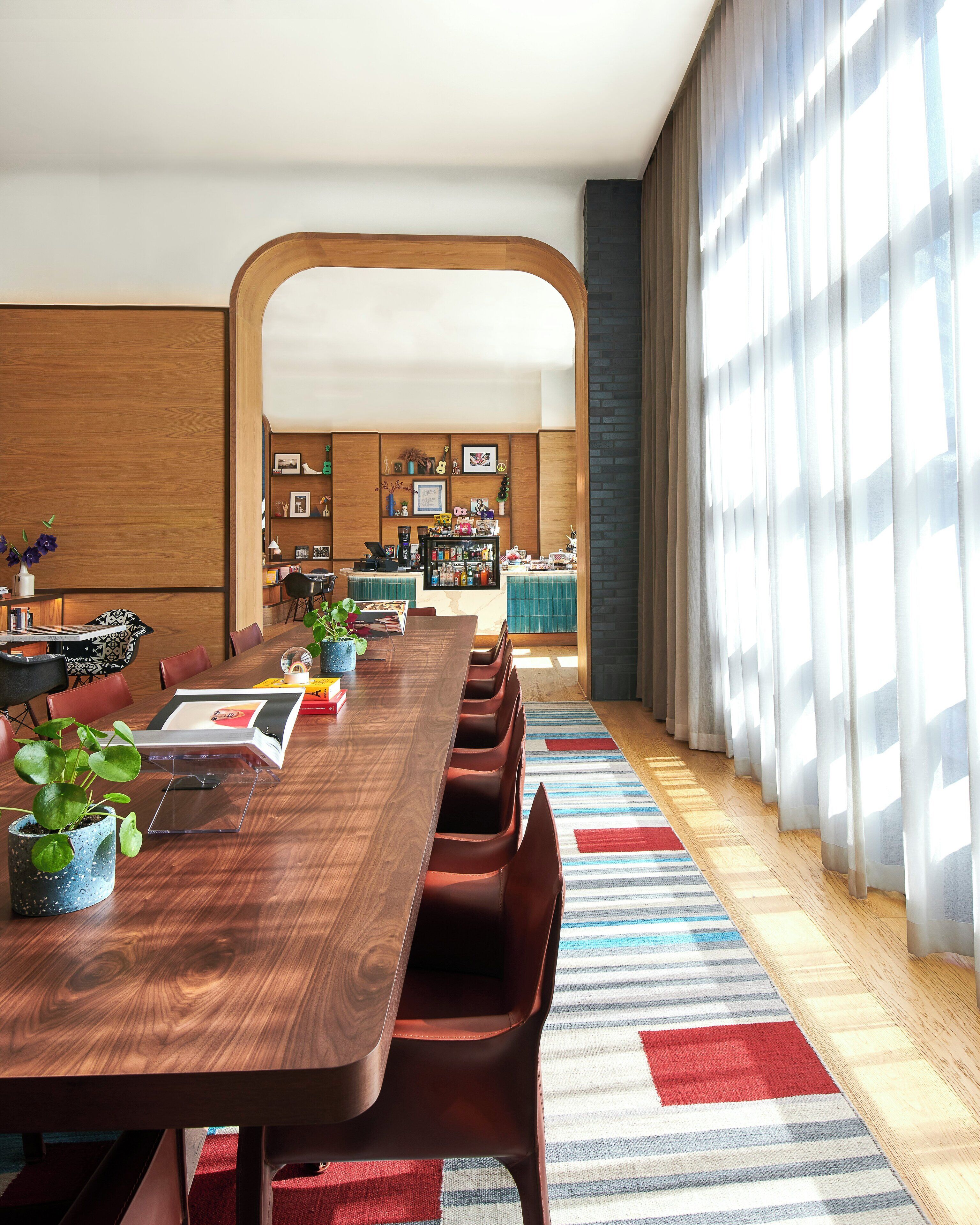 Un espace repas moderne avec une longue table en bois, des chaises rouges et un tapis à rayures.