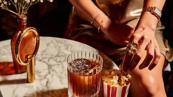 A person pouring a drink into a glass, a bottle of water, and a container of popcorn on a table.