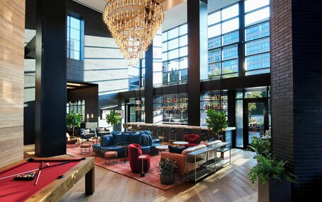 A spacious lounge area with a pool table, comfortable seating, a bar, and large windows offering views of the city.
