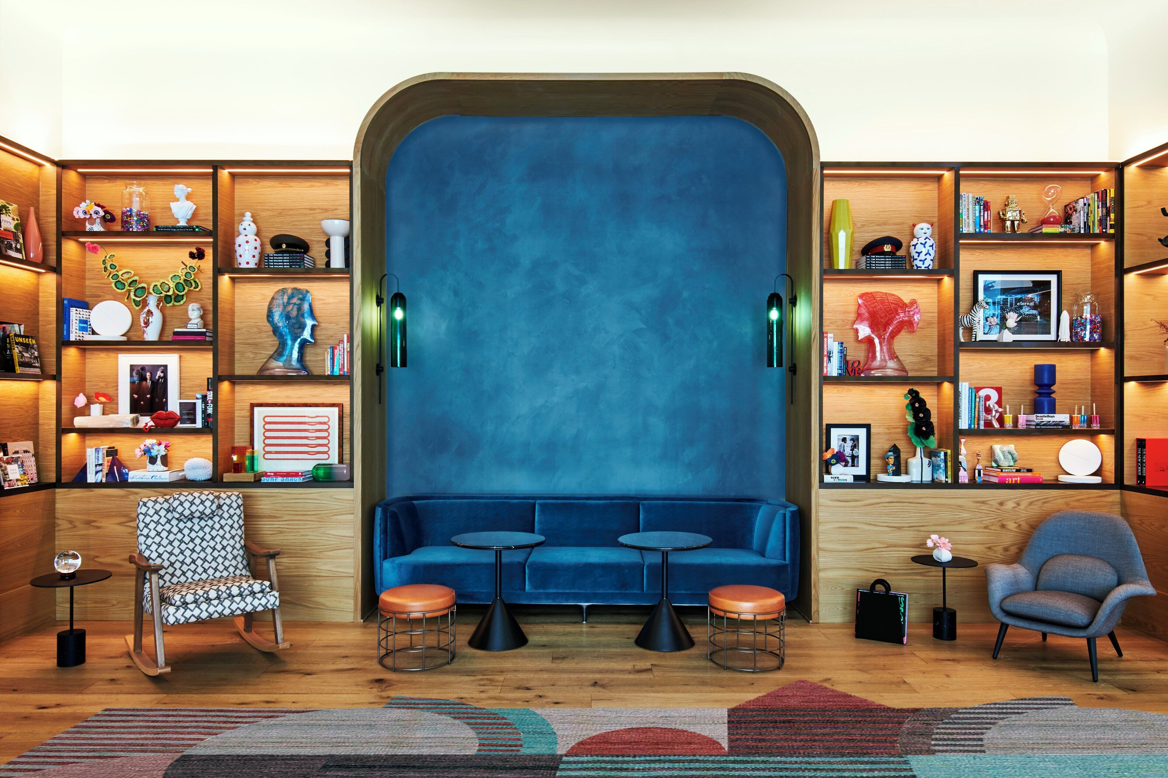 A modern living room with a blue sofa, two small tables, a patterned armchair, and a grey armchair.