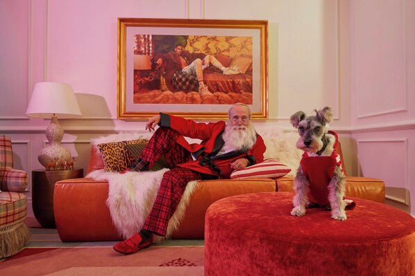 A cozy living room with a large painting on the wall, a red sofa, and a dog wearing a red sweater. - Virgin Hotels Nashville (Nashville)
