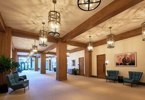 A spacious lobby with high ceilings, wooden beams, and modern lighting fixtures. There are seating areas and a large window providing natural light.
