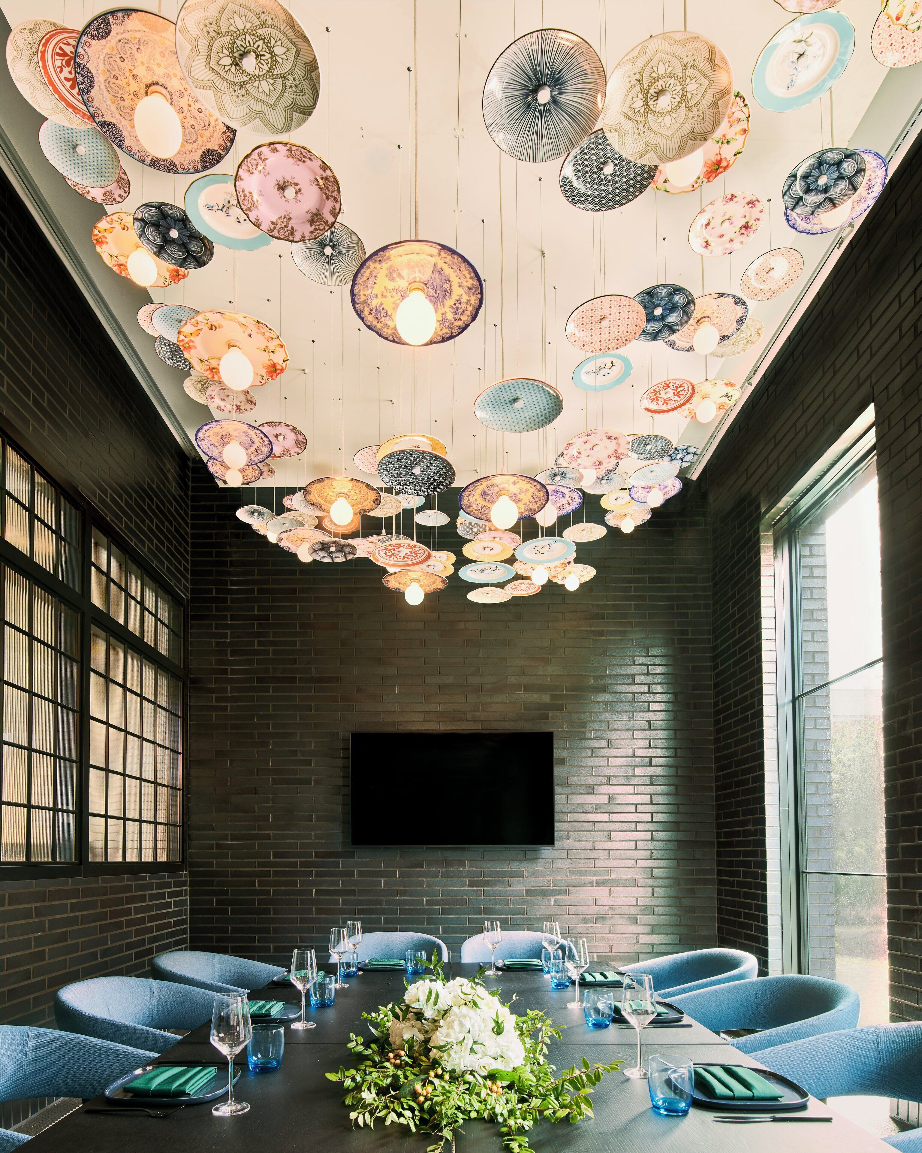 A dining area with a long table, blue chairs, and a ceiling adorned with hanging decorative plates.