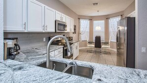 Een moderne keuken met granieten aanrechtbladen, roestvrijstalen apparatuur en witte kastjes.