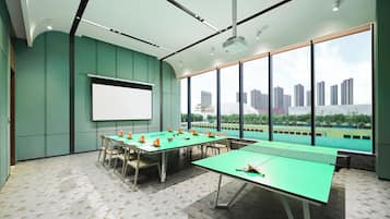 Una sala de conferencias con una gran mesa, sillas, una pantalla de proyector y vistas a un paisaje urbano a través de amplias ventanas.