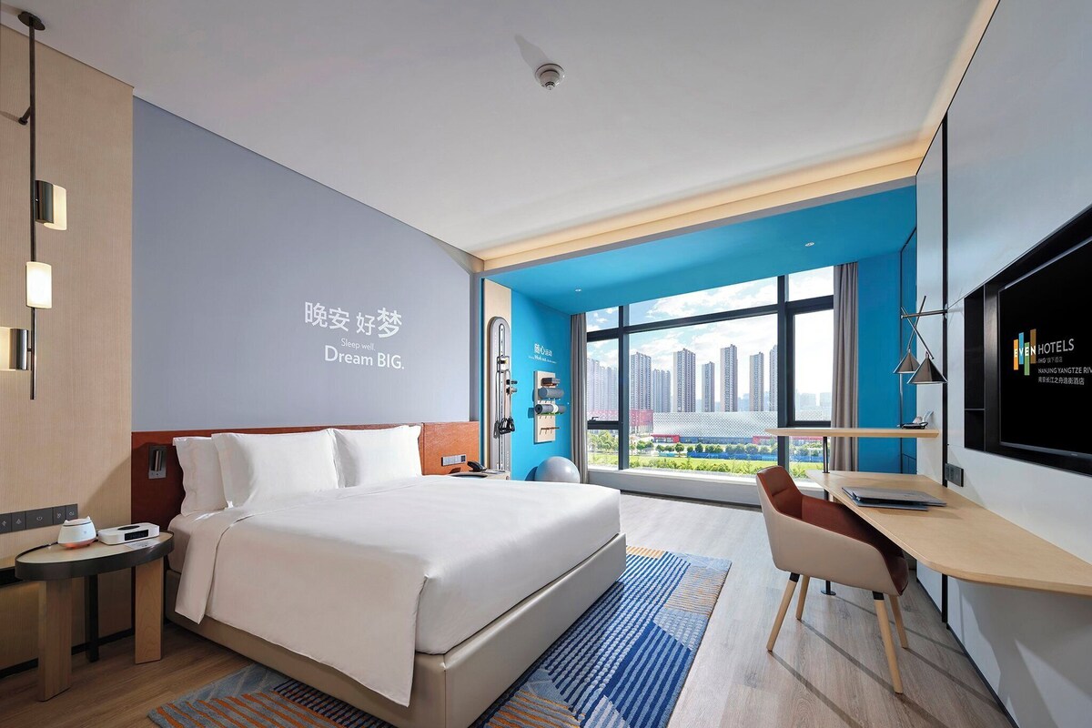 A modern hotel room with a large bed, a desk, and a TV.