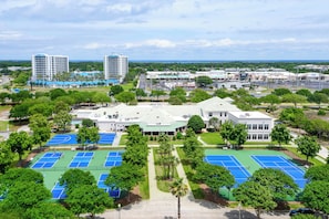 A multi-story hotel with a central courtyard, tennis courts, and surrounding greenery.