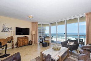 A spacious living room with a flat-screen TV, a wooden cabinet, and a view of the ocean through large sliding glass doors.