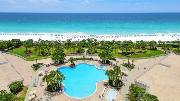 Een resort met een groot zwembad, strand en palmbomen.