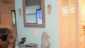 Een woonkamer met een houten console, een spiegel, een decoratie van een zeepaard en een 'WELCOME' bord aan de muur.
