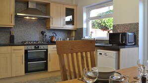 Una cocina moderna con armarios de madera, estufa, horno y microondas. Hay una mesa de comedor con sillas y una ventana con vistas a la vegetación exterior.