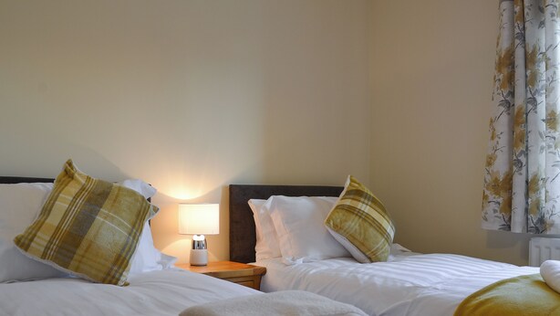 Habitación de hotel con dos camas, cada una con ropa blanca y mantas amarillas. Hay una mesita de noche con una lámpara entre las camas.