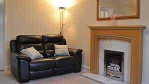 Una sala de estar con un sofá de cuero negro, dos almohadas a rayas, una lámpara de pie y una chimenea con un espejo encima.