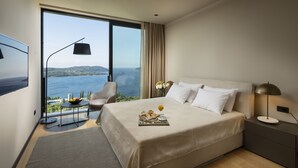 A bedroom with a large bed, a TV, a dining table with breakfast items, and a view of the sea.