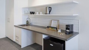 Una cucina moderna con mobili bianchi, un lavello in acciaio inossidabile, una macchina da caffè e un bollitore su una mensola.