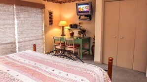 A bedroom with a bed, a desk with a chair, a television, and a wardrobe. - Fawn Valley Inn: 240 (Estes Park)
