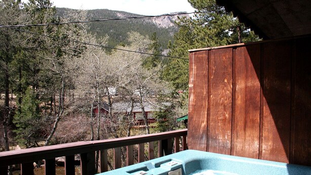 Una terraza de madera con un jacuzzi y vistas a una zona boscosa con montañas al fondo.