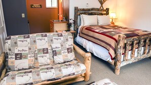 A cozy room with a wooden bed, a quilted chair, a small desk, and a welcome sign. - Fawn Valley Inn: 256 (Estes Park)