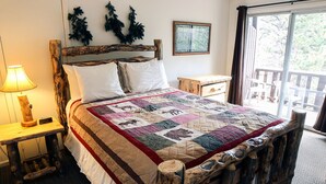 Una camera da letto rustica con un letto in legno, una coperta di trapunta, un comodino con una lampada e vista sulla natura attraverso una porta scorrevole.