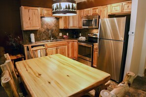 A kitchen with wooden cabinets, a stainless steel refrigerator, a microwave, and a dining table. - Fawn Valley Inn: 277 (Estes Park)