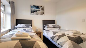 Ein Hotelzimmer mit zwei Betten, jedes mit einer Bettdecke mit geometrischem Muster, einem Nachttisch mit Lampe sowie einem Landschaftsbild an der Wand.