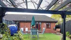Eine Terrasse mit einem Ziegelhaus, einem grünen Sonnenschirm und Gartenmöbeln.