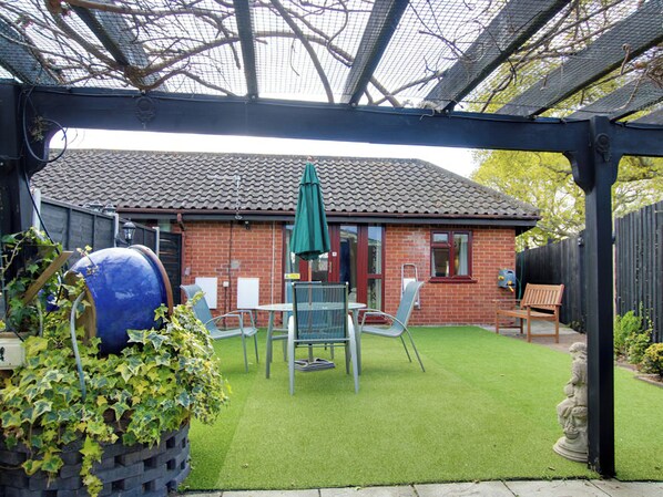 Een terras met een stenen huis, een groene parasol en tuinmeubilair.