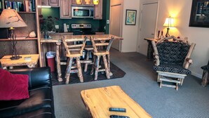 A living room with a wooden coffee table, a black leather sofa, a wooden dining table with chairs, and a patterned armchair. - Fawn Valley Inn: 280 (Estes Park)