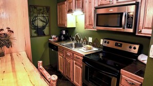 A compact kitchen with wooden cabinets, a stainless steel microwave, a stove, and a sink. - Fawn Valley Inn: 280 (Estes Park)