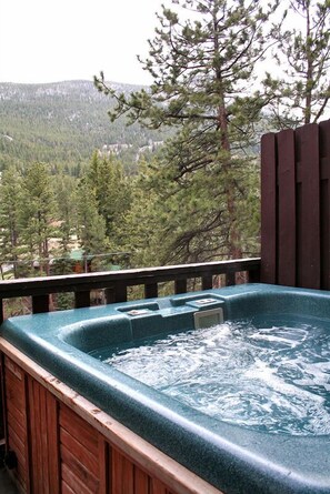 Un jacuzzi con cubierta de madera y vistas a una cadena montañosa boscosa.