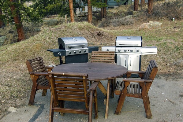 Un espacio de comedor al aire libre con una mesa redonda y sillas de madera, equipado con dos parrillas.