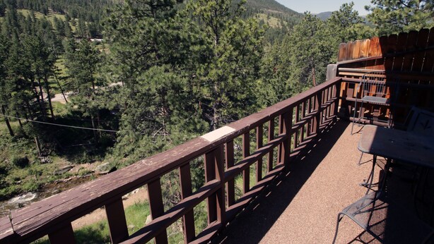 A wooden deck with outdoor seating overlooking a forested valley and a mountain. - Fawn Valley Inn: 304 (Estes Park)
