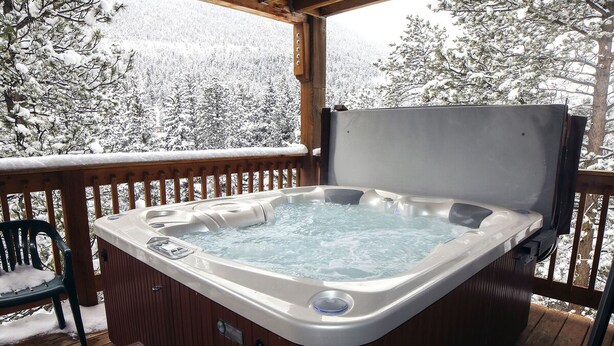 A hot tub on a wooden deck with a view of snow-covered trees. - Fawn Valley Inn: 303 (Estes Park)