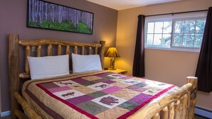 A wooden bed with a quilt, a bedside lamp, and a window with curtains. - Fawn Valley Inn: 303 (Estes Park)