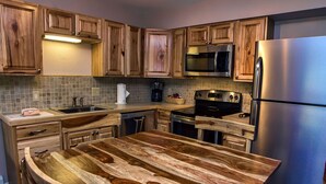 A kitchen with wooden cabinets, a stainless steel refrigerator, a microwave, a coffee maker, and a wooden island with a sink. - Fawn Valley Inn: 303 (Estes Park)