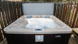 A hot tub with a control panel and a caution label, surrounded by a wooden deck. - Lazy R Cottages: 4 (Estes Park)