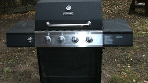 A black outdoor grill with a handle and four control knobs. - Lazy R Cottages: 7B (Estes Park)