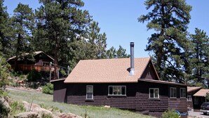 A wooden cabin with a chimney, surrounded by trees and rocks. - Lazy R Cottages: 6 (Estes Park)