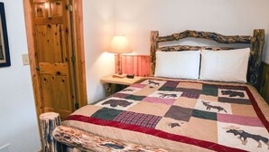 A bed with a quilt featuring animal prints, a wooden headboard, a bedside lamp, and a wooden door. - Lazy R Cottages: 8 (Estes Park)