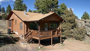 A log cabin with a wooden deck, a chimney, and a small porch. - Lazy R Cottages: 14 (Estes Park)