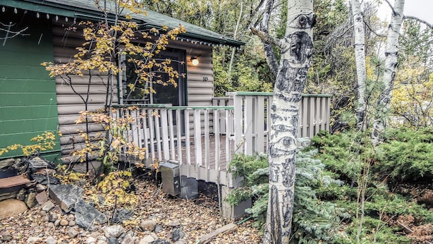 A cabin with a wooden deck, surrounded by trees and a rocky ground. - Sunnyside Knoll: 10 (Estes Park)