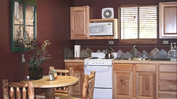 A kitchen with wooden cabinets, a white stove, a microwave, and a window with blinds. - Timber Creek Chalets: 2B (Estes Park)