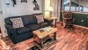 A cozy living room with a dark leather sofa, a wooden coffee table, and a rustic wooden chair.