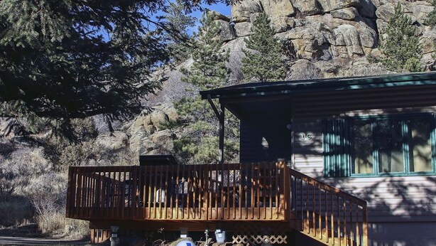A cabin with a wooden deck, a window with green trim, and a rocky mountain backdrop. - Sunnyside Knoll: 16 (Estes Park)